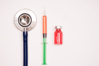 Directly above shot of stethoscope by syringe and medicine bottle over white background