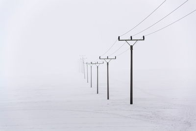 Electricity pylons on wooden post against sky during winter