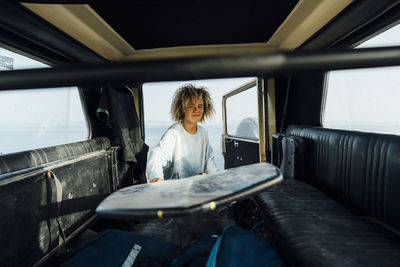 Smiling woman removing surfboard from car while standing at beach