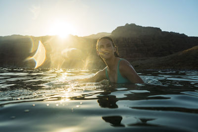 Woman swimming in sea against mountain during sunset