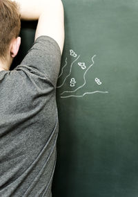 Rear view of man standing against blackboard representing sweat