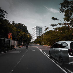 Cars on road by buildings against sky in city