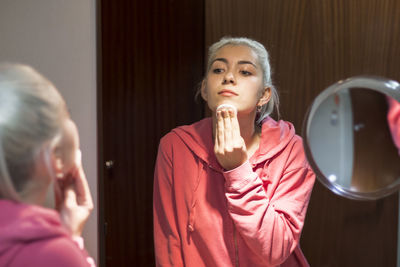 Smiling young woman applying make up in bathroom