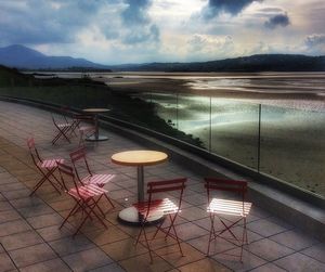 Chairs and table by sea against sky