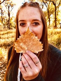 Portrait of young woman holding dry leaf in park during autumn