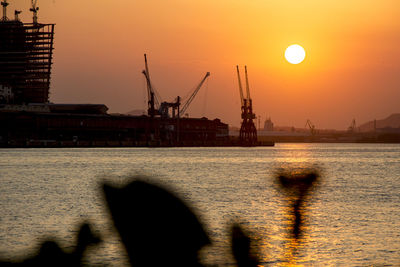 Silhouette cranes at commercial dock against sky during sunset