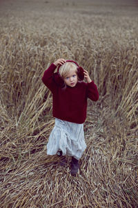 Girl in a red sweater stands on a field of wheat in the autumn