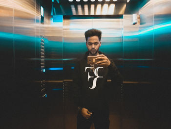 Young man using mobile phone in illuminated room