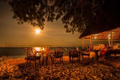 Chairs and table on beach against sky during sunset