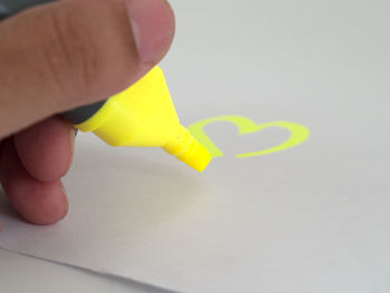 Close-up of hand holding yellow paper over white background