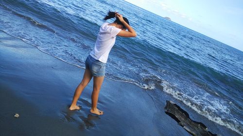 Rear view of young woman fixing hair at beach