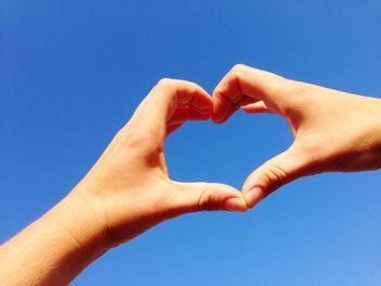 Low angle view of hand making heart shape against clear blue sky