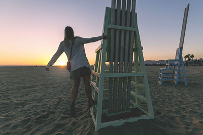 Rear view of woman standing on beach against sky during sunset