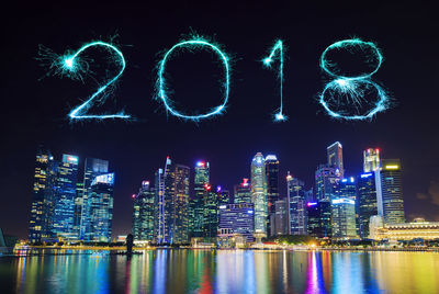 Illuminated city by river against sky at night