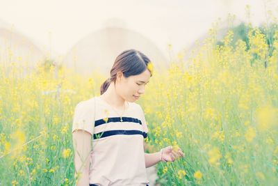 Thoughtful young woman standing amidst yellow flowering plants on field