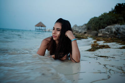 Teenage girl lying on shore at beach against sky