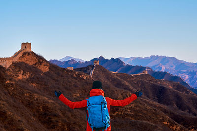 Rear view of man standing on mountain against blue sky