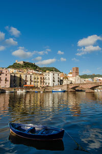 Boats moored in canal by buildings against blue sky