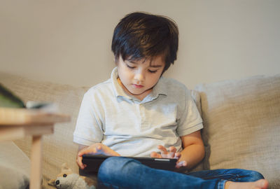 Boy looking away while sitting on sofa at home