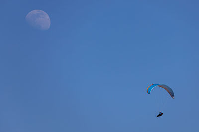 Low angle view of person paragliding against blue sky