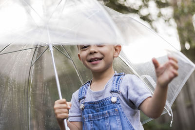 Portrait of happy boy holding umbrella while standing outdoors during rainy season