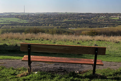 Empty bench on field by trees against sky