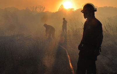 Men in protective workwear standing on field during sunset