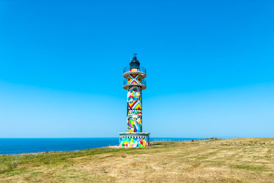 Lighthouse by sea against clear blue sky