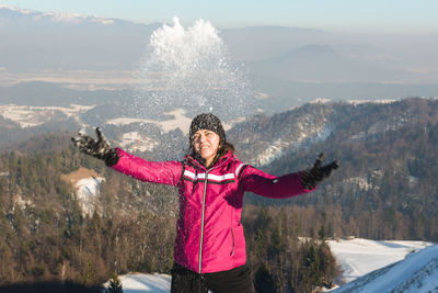 Woman playing with snow against mountains