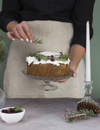 The girl's hands decorate the christmas cake with rosemary on a gray table.