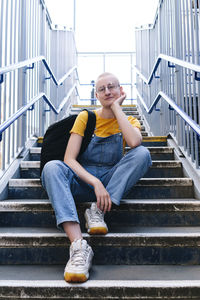 Androgynous person with backpack sitting on staircase