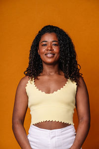 Portrait of young woman standing against yellow background