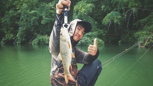 Young man holding fish by lake