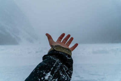 Male hand reaching out into fog and snow-covered landscape with mountains and pines.