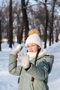 A girl in warm clothes wants to throw a snowball in a winter park. outdoor games.