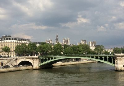 Bridge over river by buildings against sky in city