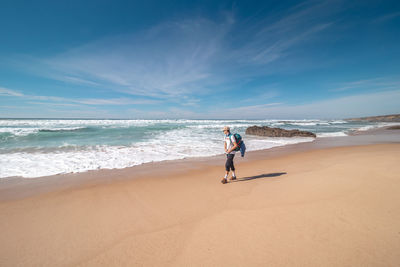 Rear view of woman walking at beach against sky