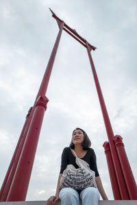 Low angle view of woman sitting on playground against sky