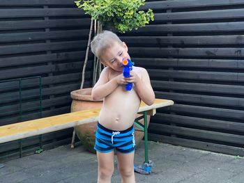 Shirtless boy playing with squirt gun against wall