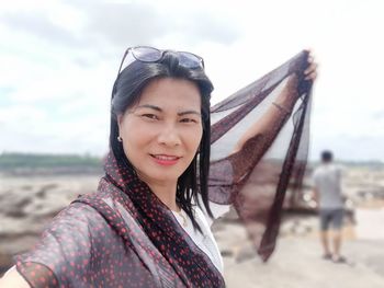 Portrait of smiling young woman standing on beach against sky