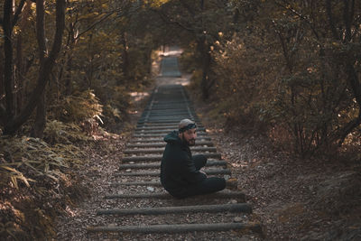 Side view of man sitting on staircase in forest
