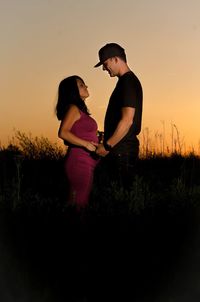 Side view of couple standing against sky during sunset