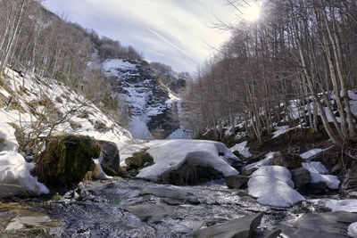 Scenic view of river amidst snow covered rocks in forest