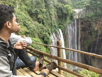 Man friends looking at waterfall while sitting at observation point