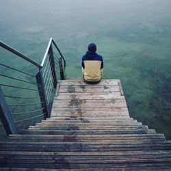 Rear view of person sitting on wooden steps by sea