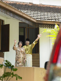 Couple waving while standing outside house
