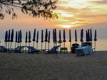 Chairs on beach against sky during sunset