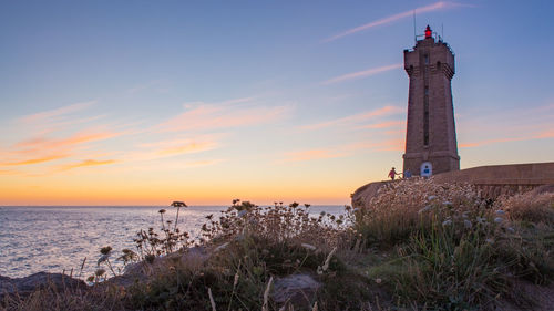 Lighthouse by sea against sky during sunset