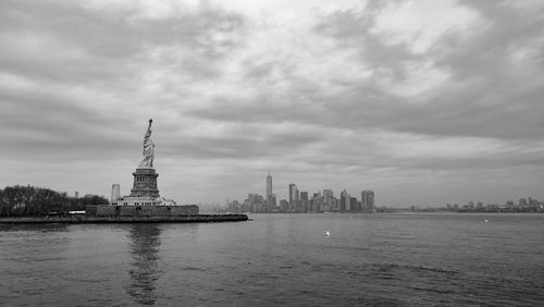 Statue of city at waterfront against cloudy sky
