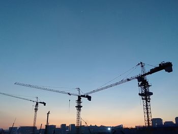 Low angle view of cranes at construction site against sky during sunset